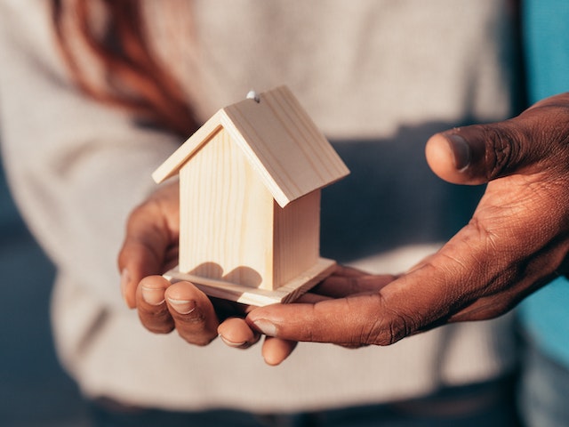 a-person-holding-a-small-wooden-model-of-a-house